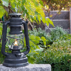 Feuerhand Baby Special 276 Sturmlaterne leuchtet in einem Garten mit grünem Laub.