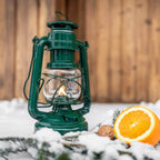 Feuerhand Baby Special 276 Sturmlaterne auf Schnee mit orange und Tannenzweigen im Hintergrund
