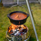 Feuertopf (Dutch Oven) mit dampfendem Eintopf über offenem Feuer im Garten.