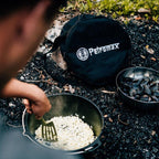 Transporttasche Feuertopf & Grill neben einem Dutch Oven bei einem Koch-Abenteuer im Freien.