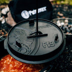 Deckelheber für Feuertopf in Aktion zur sicheren Handhabung heißer Feuertopfdeckel beim Kochen im Freien.
