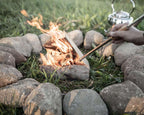 Feuerrohr von Petromax wird verwendet, um ein Feuer in der Natur zu entzünden, umgeben von Steinen und Rasen.