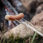 Lagerfeuer-Spieß mit Bratwurst über offenem Feuer, ideal zum Grillen von Würstchen und anderen Speisen.
