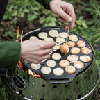 Zubereitung von Poffertjes in der Poffertjespfanne über einem Lagerfeuer, 30 Mini-Pfannkuchen gleichzeitig.