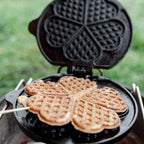 Waffeleisen mit frisch gebackenen Waffeln in Herzform, ideal für das Backen im Freien.