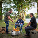 Drei Freunde genießen ein Grillabend mit einer Feuerschale Tyropit am Wasser.