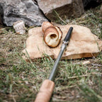 Stockbrot Spieß mit Gusseisenspitze neben Stockbrot auf Holzbrett im Freien.
