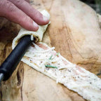 Stockbrot Spieß mit Gusseisenspitze wird mit Teig gefüllt und auf einem Holzbrett vorbereitet.