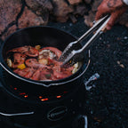 Atago Black Edition cooking shrimp in a black pot on a portable grill with tongs.