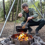 Ein Mann kocht im Freien mit einem Feuertopf (Dutch Oven) über offenem Feuer in der Natur.